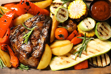 Delicious barbecued steak served with garnish and sauce on wooden board, top view