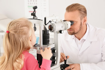 Fototapeta premium Children's doctor examining little girl with ophthalmic equipment in clinic