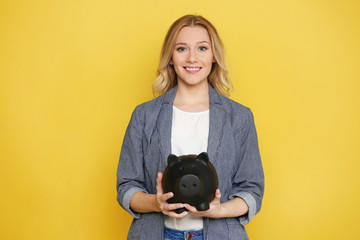 Happy young woman with piggy bank on color background