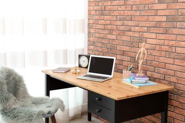 Stylish workplace interior with laptop on table near brick wall. Space for text
