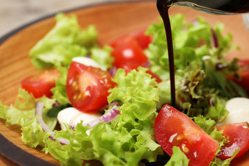 Pouring balsamic vinegar onto fresh vegetable salad on plate, closeup