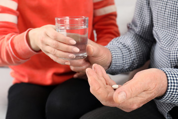 Woman giving glass of water to senior man with pill, closeup