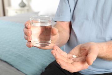 Senior man holding pill and glass of water indoors, closeup