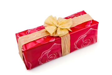 Gift box wrapped in red rose cellophane, decorated with ecru raffia ribbon and bow isolated on the white background