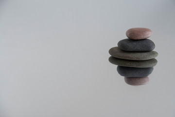 Pyramids of gray zen pebble meditation stones with green leaves on the mirror water reflection background. Concept of harmony, balance and meditation, spa, massage, relax