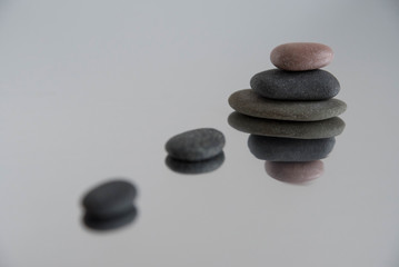 Fototapeta na wymiar Pyramids of gray zen pebble meditation stones with green leaves on the mirror water reflection background. Concept of harmony, balance and meditation, spa, massage, relax
