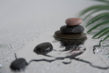 Pyramids of gray zen pebble meditation stones with green leaves on the mirror water reflection background with water splash. Concept of harmony, balance and meditation, spa, massage, relax