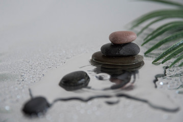 Pyramids of gray zen pebble meditation stones with green leaves on the mirror water reflection background with water splash. Concept of harmony, balance and meditation, spa, massage, relax