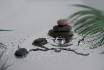 Pyramids of gray zen pebble meditation stones with green leaves on the mirror water reflection background with water splash. Concept of harmony, balance and meditation, spa, massage, relax
