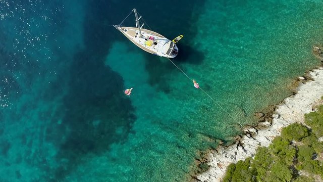 Aerial view of two women floating on inflatable next to sailing boat, Greece.