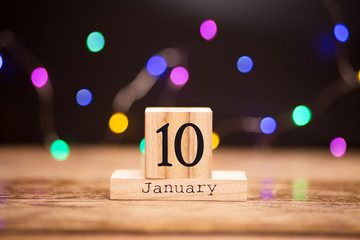 Naklejka premium January 10th. Day 10 of January set on wooden calendar on dark background with garland bokeh. Winter time. Holiday Composition