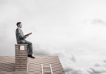 Student guy in suit on brick house roof reading book