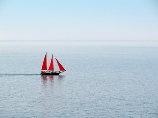 A boat with three red sails, floating on clear sea background