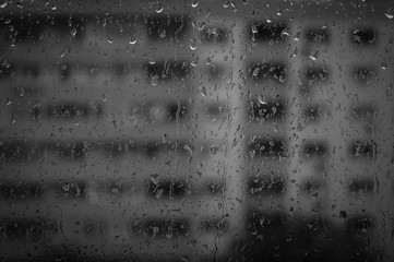 Rain drops on window, reflecting city buildings. Black and white