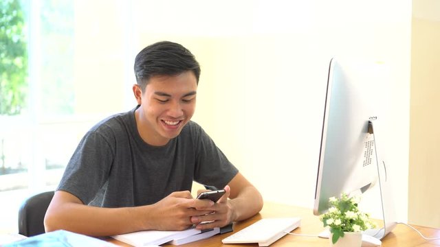 Student learning online study concept: Asian Young man sitting holding smartphone chatting in home for e-learning in educational technology by self