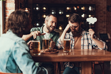 Cheerful young men with drinks having fun at pub