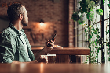 Bearded man using cellphone while spending time at pub