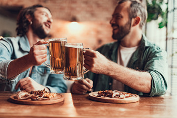 Two cheerful men toasting with beer at pub