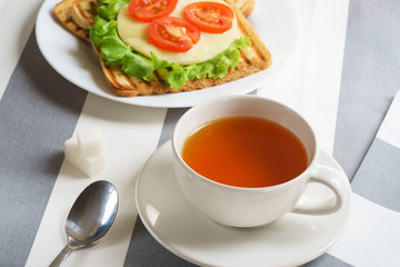 Fresh, tasty breakfast with a sandwich and tea on a light background.