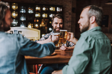 Young men toasting with drinks while spending time at pub