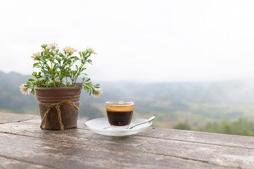 Morning cup of coffee and Flower Pot on the wooden table with mountain background at sunrise and sea of mist, image with copy space.