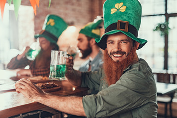 Cheerful young man celebrating Saint Patrick Day with friends at pub