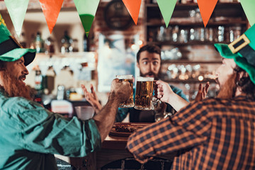 Cheerful friends toasting with mugs of beer at pub