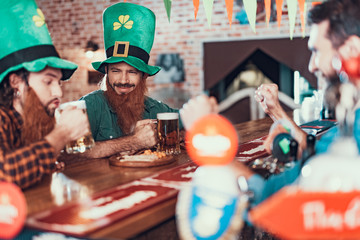 Cheerful men in costumes of leprechaun drinking beer in pub