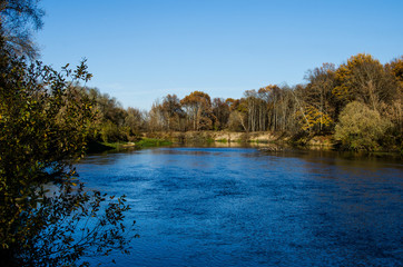 The flow of the river blurs the shore. Autumn landscape with a misty river with steep wooded banks