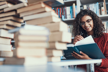 Waist up of happy student reading near the pile of books