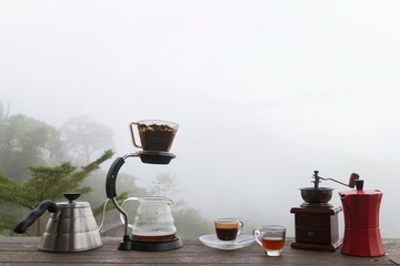 Morning cup of coffee with Rotary Coffee Grinder on the wooden table with mountain background at sunrise and sea of mist, image with copy space.