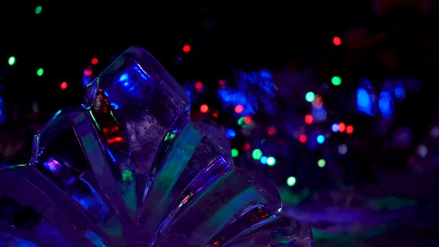 New Year. Christmas. Celebration. Beautiful illumination of colored lights in the form of bokeh. Sculpture of transparent ice.