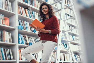 Confident lady smiling while sitting on the step ladder with orange book