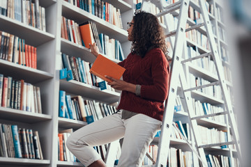 Careful lady taking books from the library bookcase