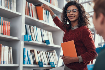 Pretty curly lady smiling and taking books from the shelf