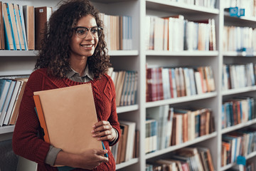 Waist up of positive student standing in the library and looking happy