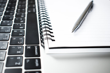 A close up photograph of a pen placed in a notebook and a computer of a young businessman.
