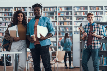 Waist up of three students standing in the library and smiling