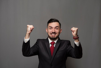 Portrait of an emotional happy businessman rejoicing at something and showing yes on gray background