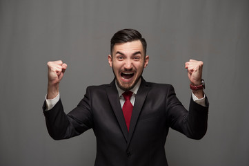 Emotional businessman in formal suit shouting with joy raising his hands