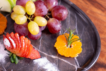 fruit plate. strawberry, grape, mandarin, orange, grapefruit, pineapple, peppermint in marble plare on wooden table