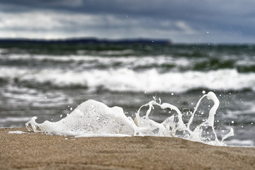 A small wave breaks on the Baltic Sea beach in front of a contrasting sky, the spray and single...