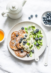 Served breakfast or dessert - whole wheat pancakes with greek yogurt, blueberries, kiwi, honey and nuts on a light background, top view. Flat lay