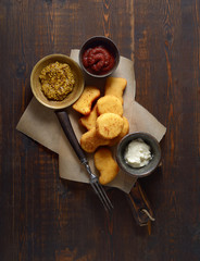 Fried chicken nuggets with white sauce, mustard and ketchup on a dark wooden background. Top view.