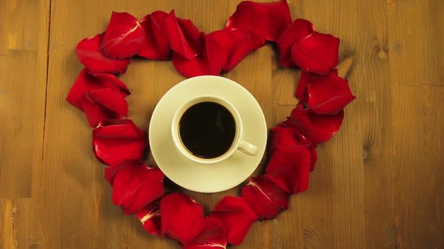 The girl puts in the middle of the heart of rose petals a cup of coffee.