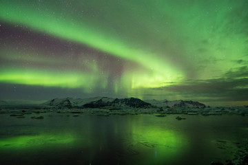 Fototapeta na wymiar Northern Lights over frozen glacier lake and mountains in Iceland winter
