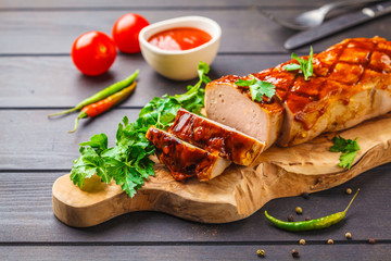 Baked meatloaf with greens and barbecue sauce on a wooden board, dark background.