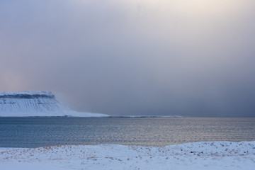 Seascape in Iceland with stormy sky over snow-covered mountain on coast in winter