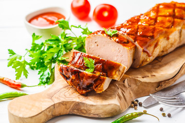 Baked meatloaf with greens and barbecue sauce on a wooden board, white background.