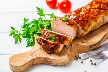 Baked meatloaf with greens and barbecue sauce on a wooden board, white background.